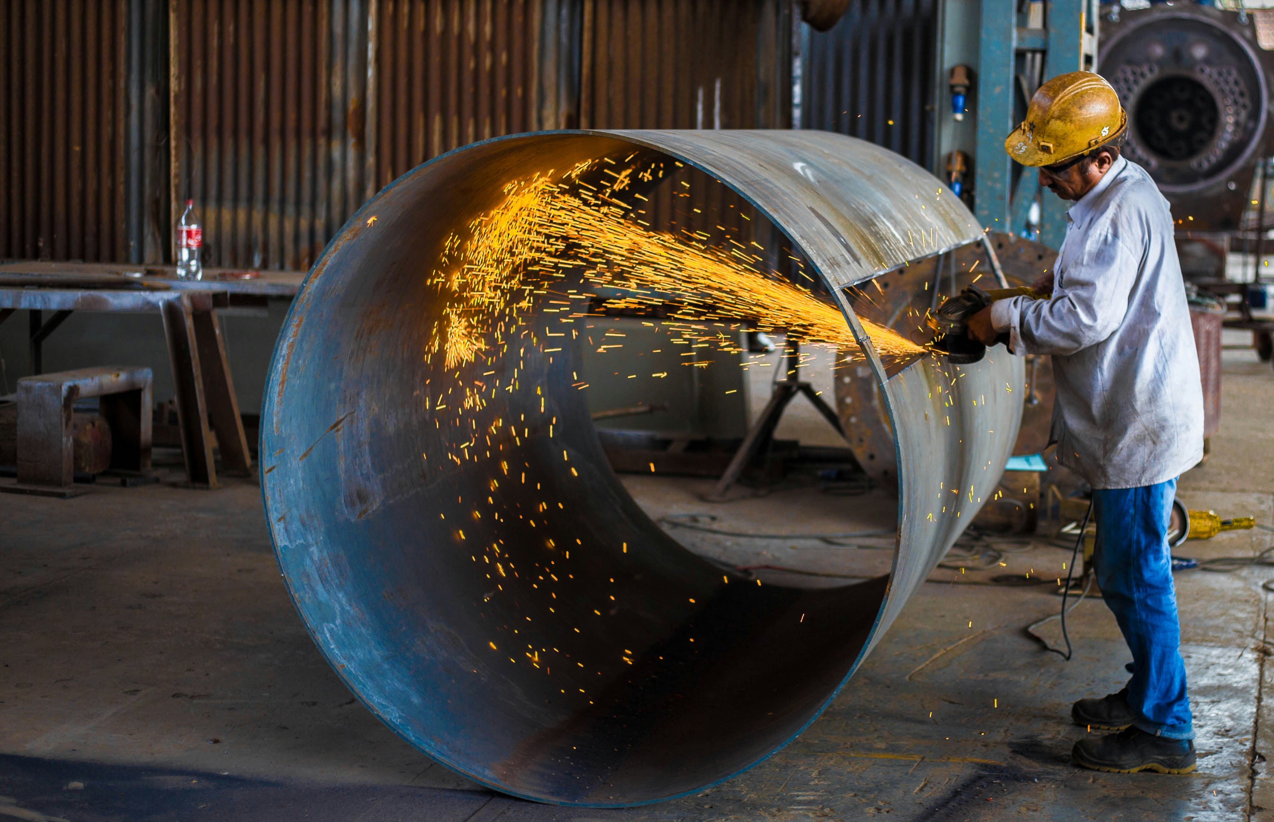 Fabricator cutting a large steel pipe, sparks flying across the shop floor